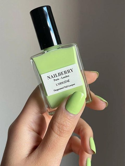 Eine Hand erischtlich, die die grüne Nagellack Flasche von Nailberry hält. Die Farbe vom Nagellack ist Hellgrün.