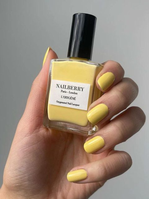 Eine Hand hält die gelbe Nagellack Flasche mit schwarzer Kappe von der Marke Nailberry