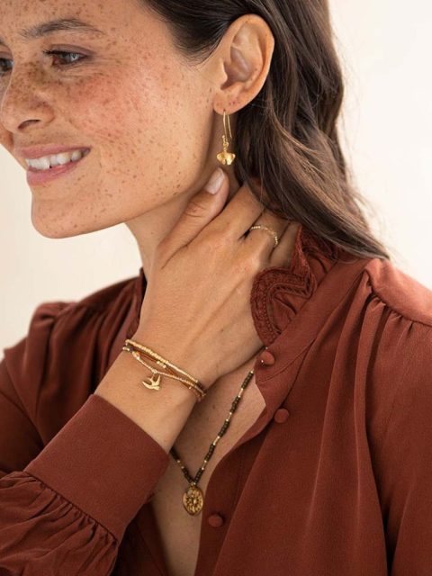 Modell trägt Halskette, die auch als Armband getragen werden kann in Rot-Braun-Gold Tönen und Vogel Anhänger.