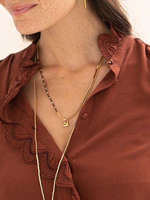 Modell trägt Halskette, die auch als Armband getragen werden kann in Rot-Braun-Gold Tönen und Vogel Anhänger.