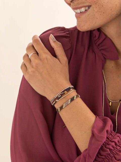 Modell trägt Armband in Rosa, Gold und Rot-Violetten Tönen mit kleinen Anhänger in Gold