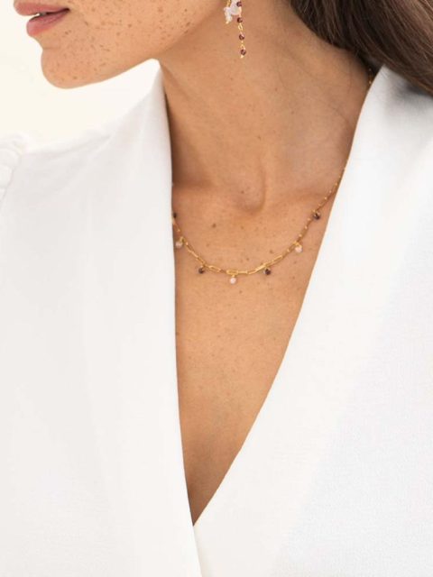 Das Modell trägt eine Halskette aus goldigen Kettenmuster. Die Kette hat mehrere kleine Granat und Rose Quartz Anhänger. Die Kette ist handgemacht von der Marke a beautiful story