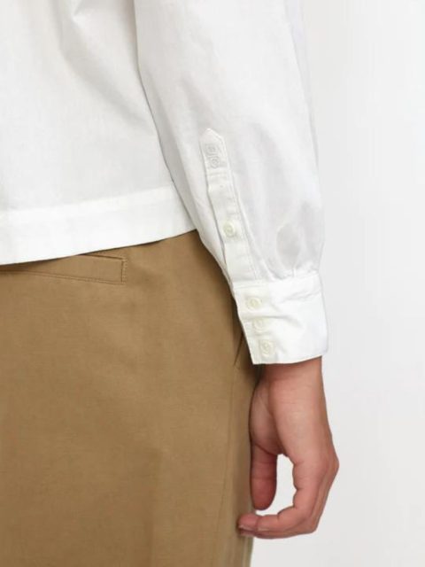 Nahaufnahme von Modell, die eine Bluse in Weiss trägt zusammen mit einer hellbraunen Hose. Ihre Hand ist ersichtlich, die Finger sind locker gekrümmt
