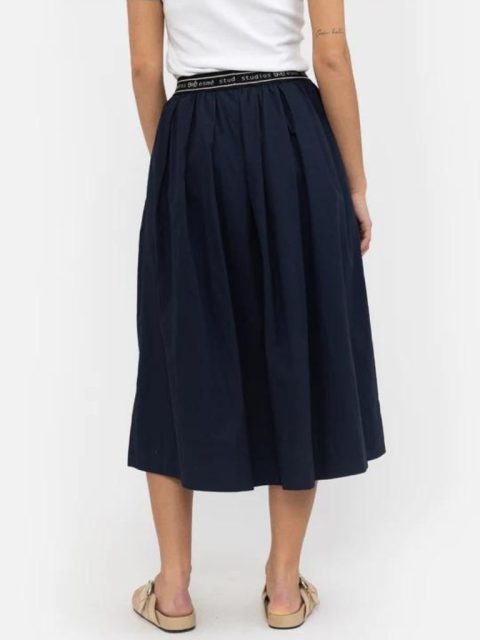 Modell von hinten, vom Rücken abwärts ersichtlich. Sie trägt ein lockeres T-Shirt in Weiss, mit einem dunkelblauen Jupe, welches ein Elastikband hat, die mit 