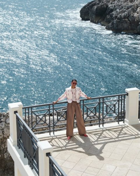 Frau steht mit langer, fliessender Stoffhose in braun am Meer. Skandinavischer Style. Sommermode